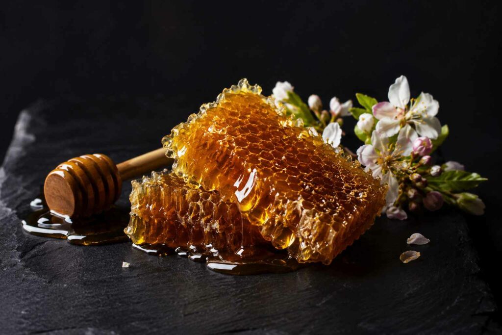 Des morceaux de rayons de miel frais et dorés sur une ardoise noire avec une cuillère en bois, une mise en scène idéale pour valoriser un miel clair comme l’acacia.